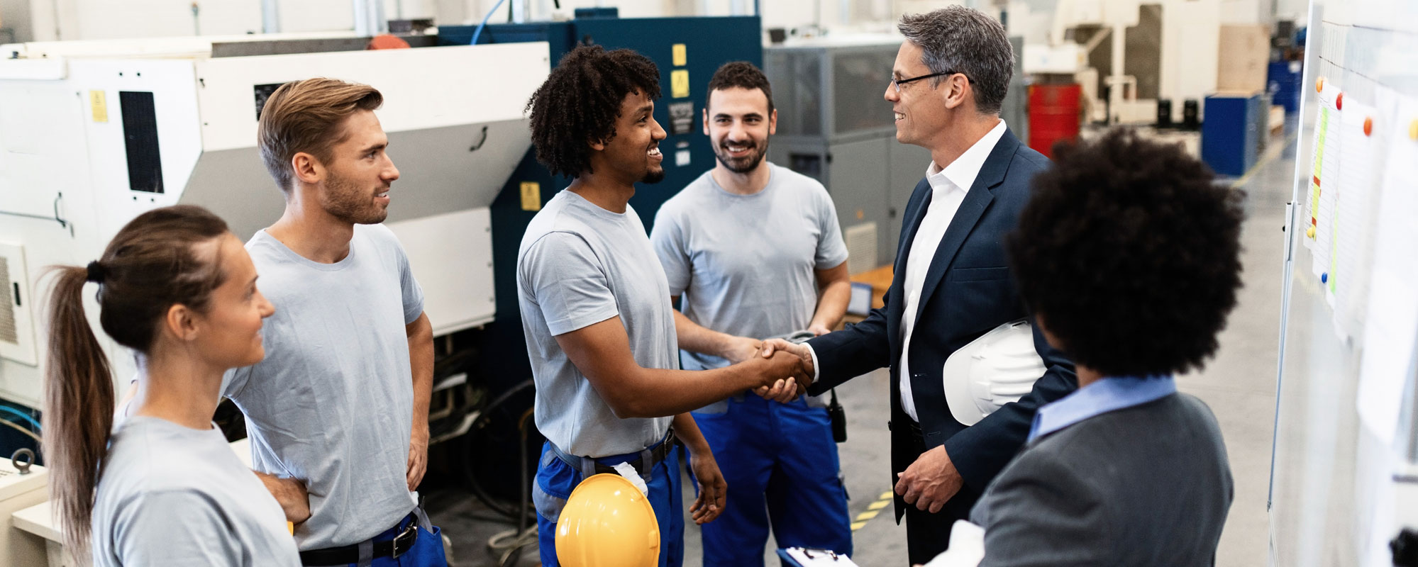 A supervisor shaking hands with one of his employees surrounded by a group of employees.
