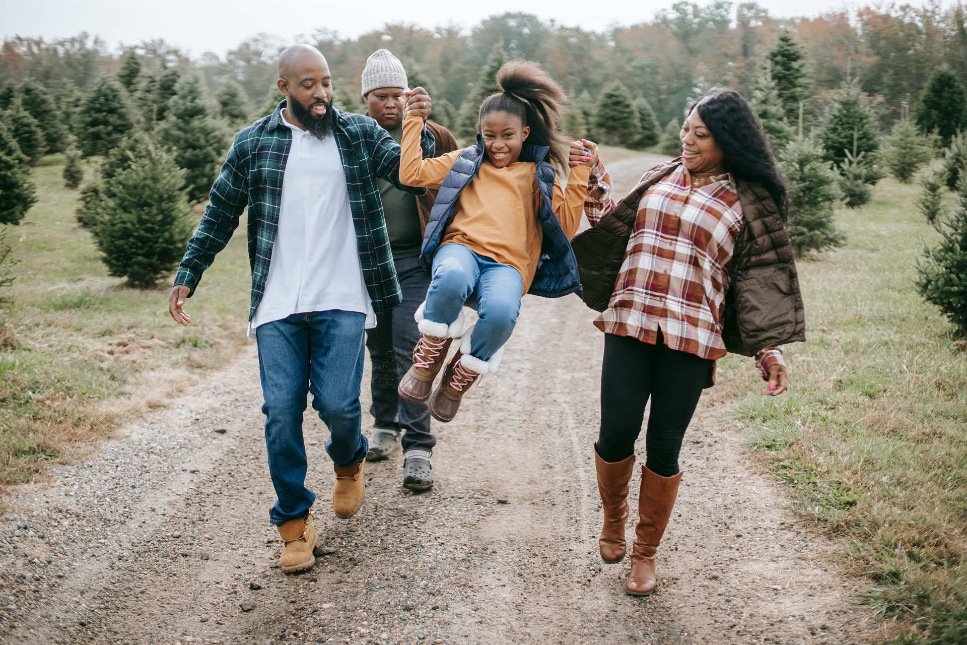 African-American parents walking on trail and lifting their young daughter off the ground to her delight.