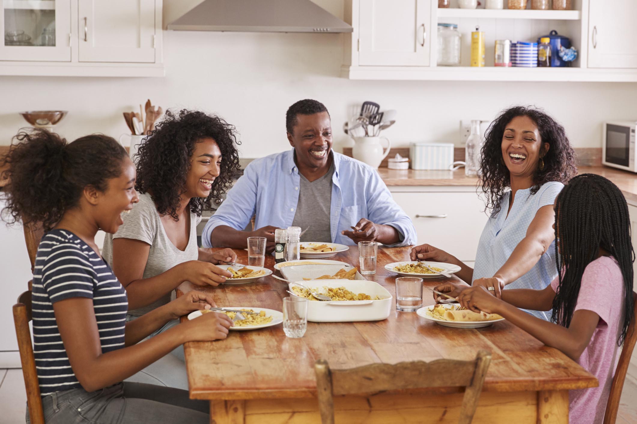 Family With 3 Teenage Children Eating Meal In Kitchen.