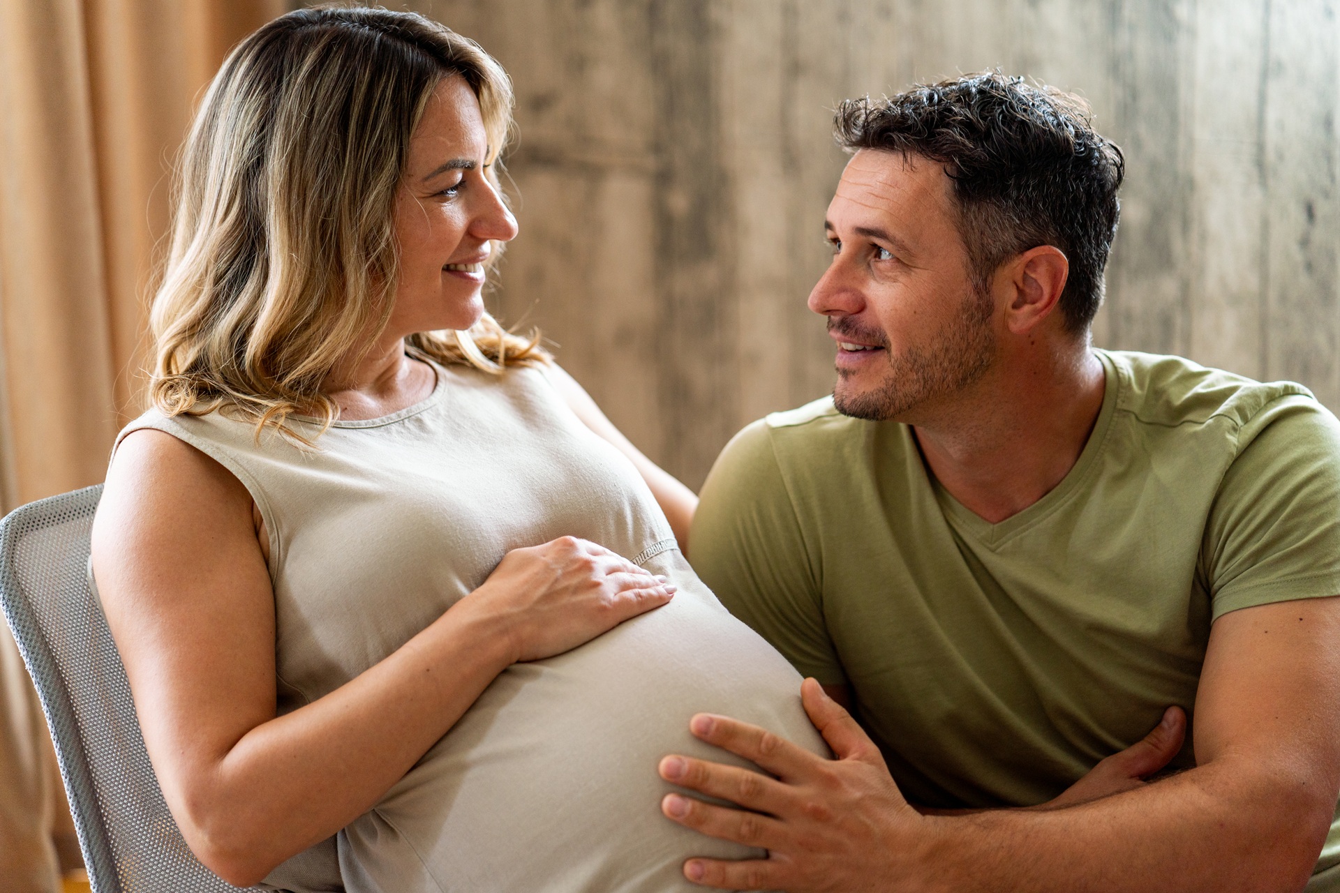 A pregnant woman laying down as her husband crouches beside her and touches her stomach..