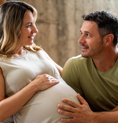 A pregnant woman laying down as her husband crouches beside her and touches her stomach..