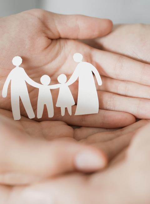 Two pairs of hands cradling a paper cutout family.