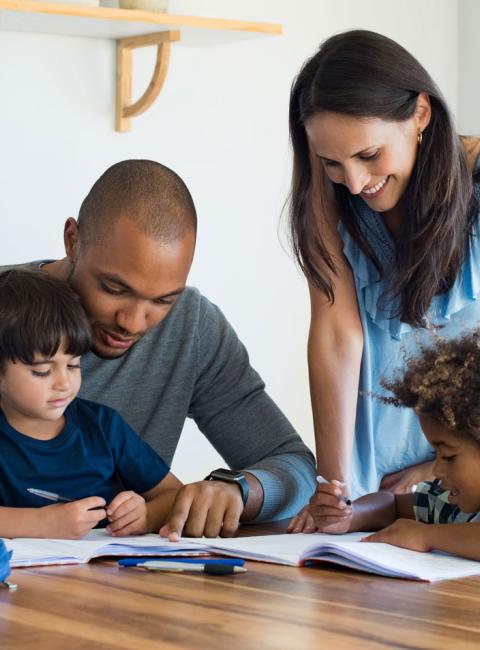 Parents helping two sons with homework at the dinner table.