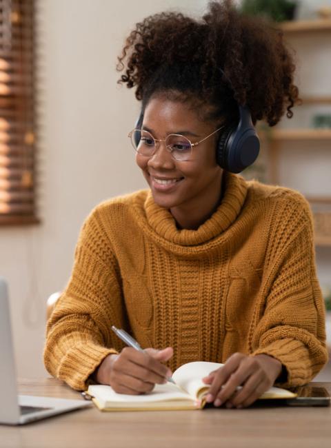 Young woman taking notes in her book while watching her computer.